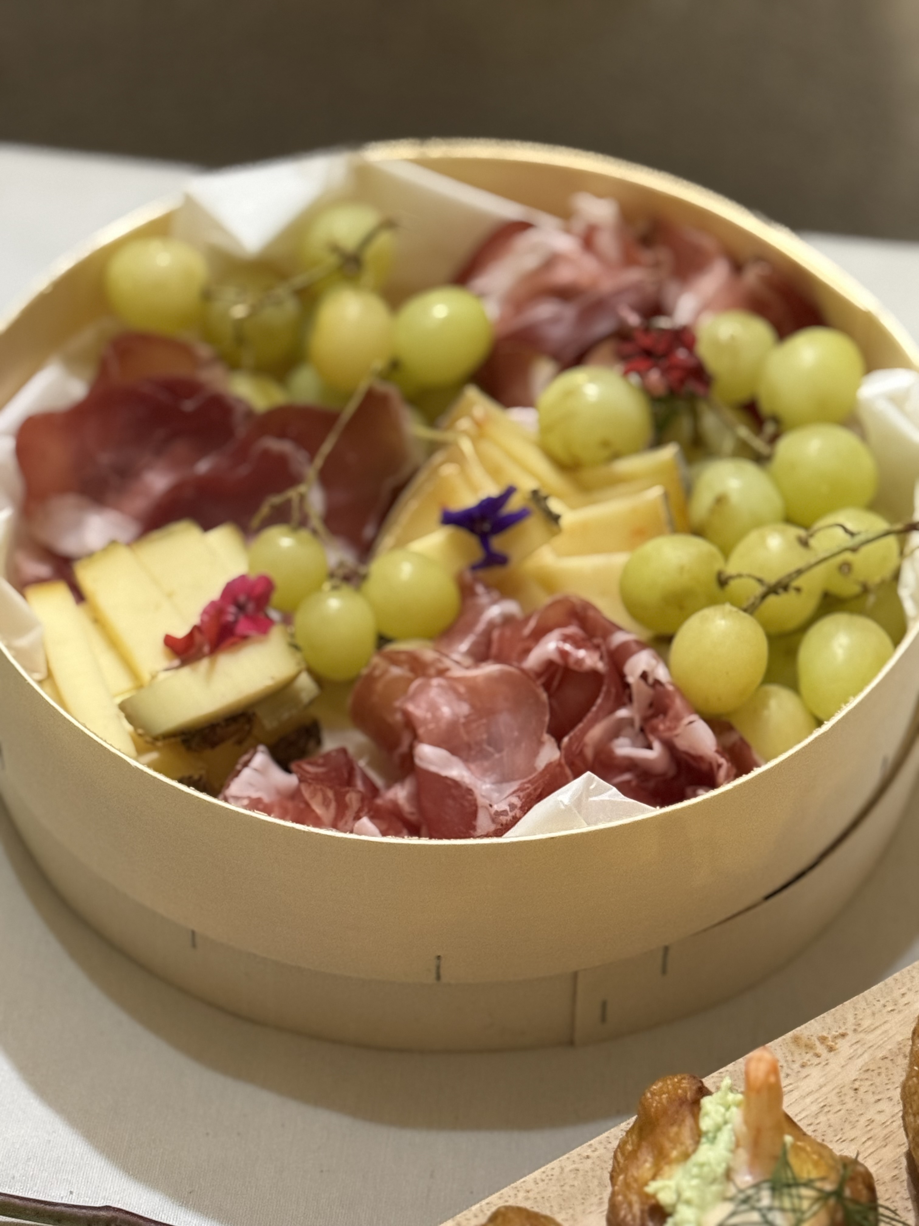 Box ronde grazing avec charcuterie, fromage, raisin et fleurs comestibles
